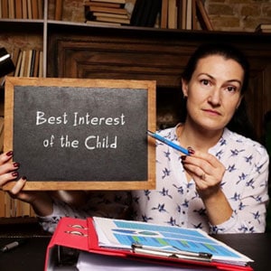 A woman holds a blackboard with the words best interest of the child written on it - Michael Cochran Law Offices